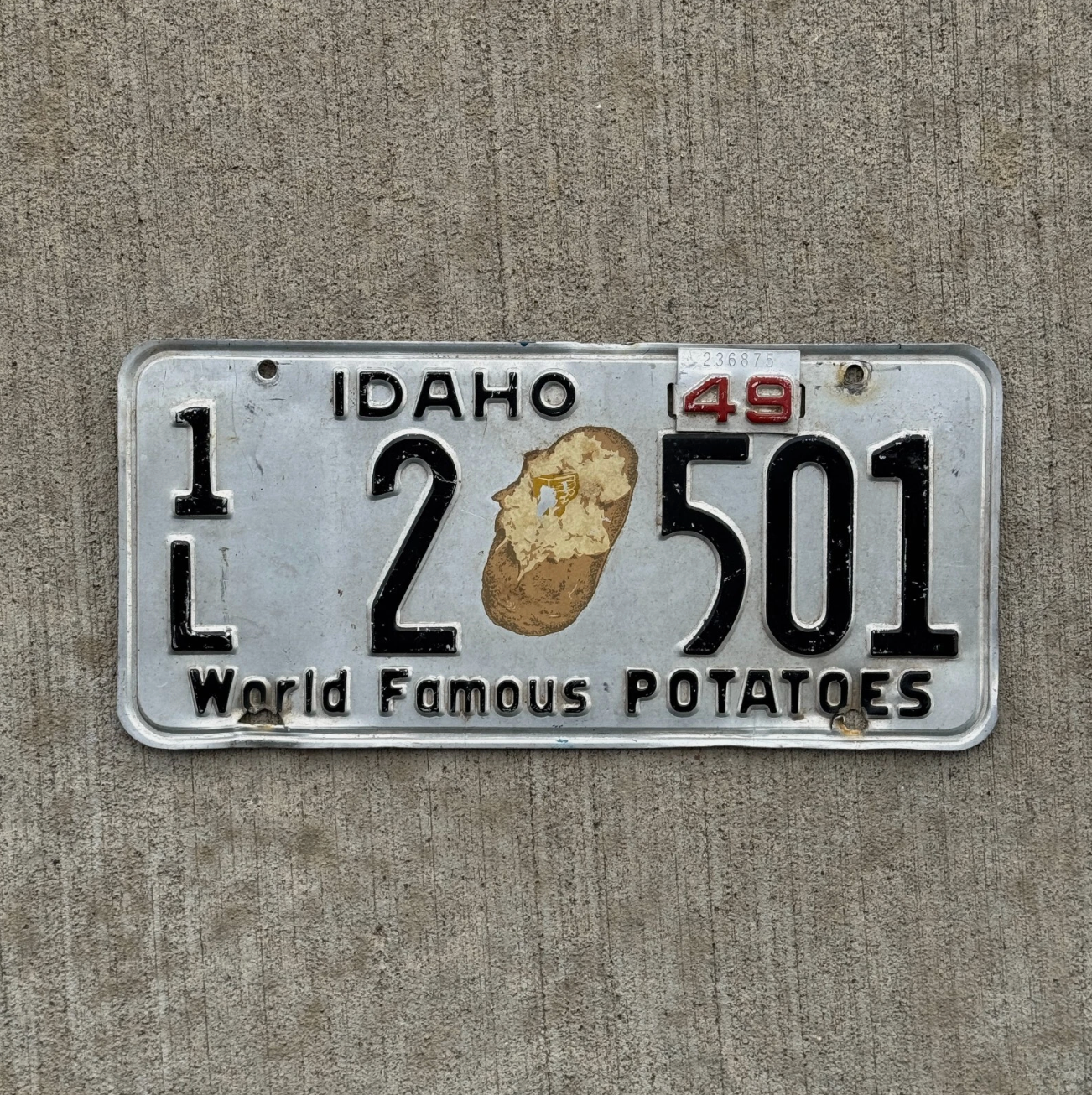 Vintage Idaho license plate with iconic potato graphic and the number 1L 2 501. Plate displayed on a concrete background.