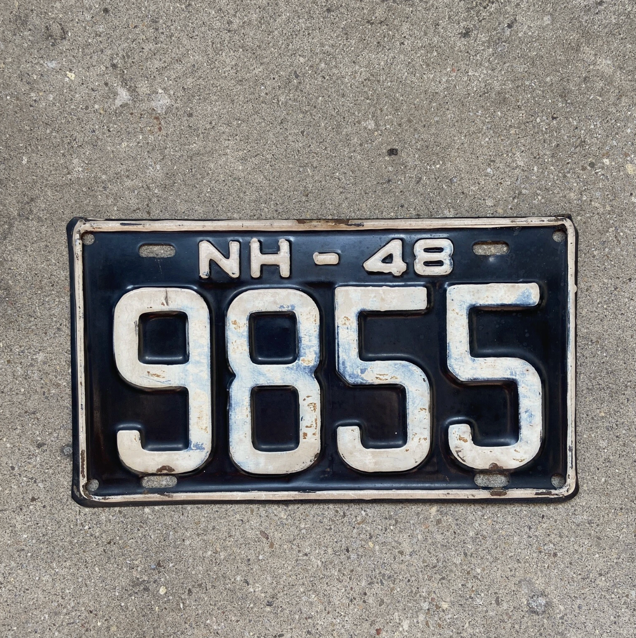 Vintage 1948 New Hampshire license plate with registration number '9855' on a concrete surface