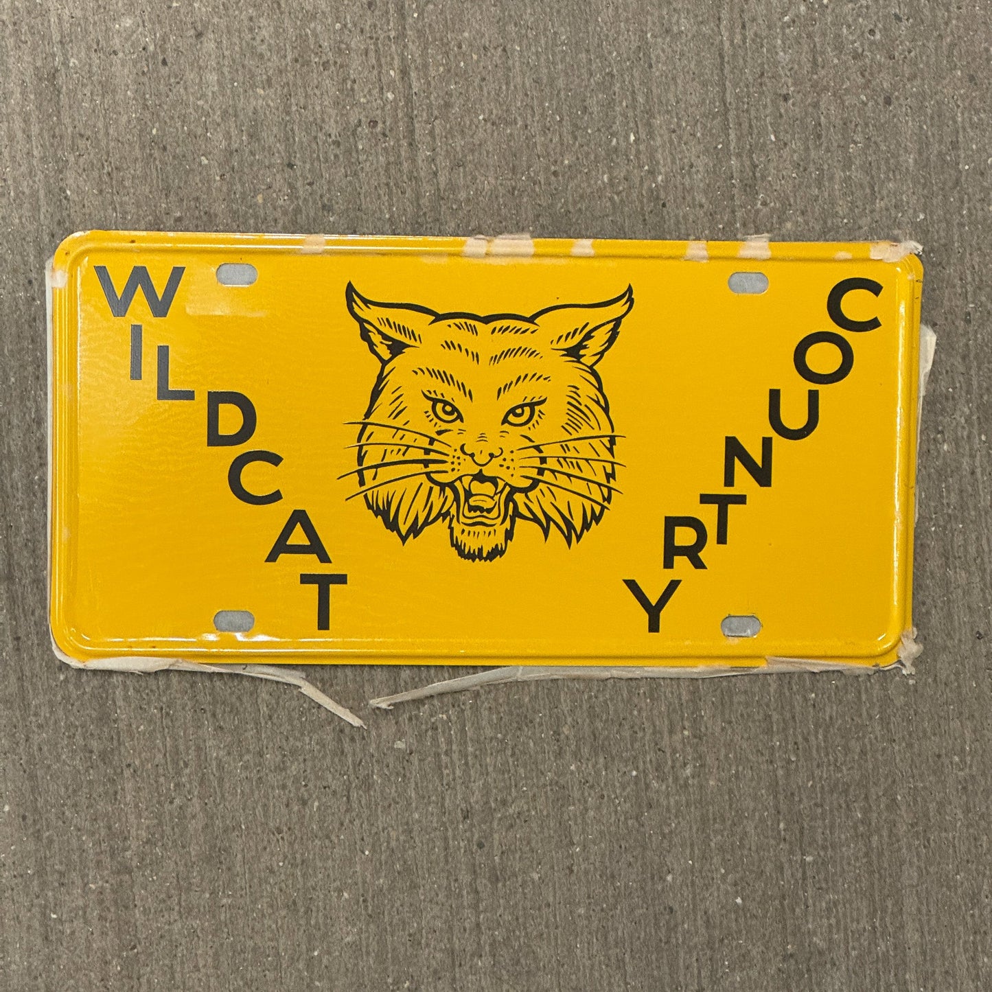 Photo of a 1950 Era Booster License Plate Auto Tag 1 Garage Decor New Old Stock with Rice Paper Wildcat Country with original patina