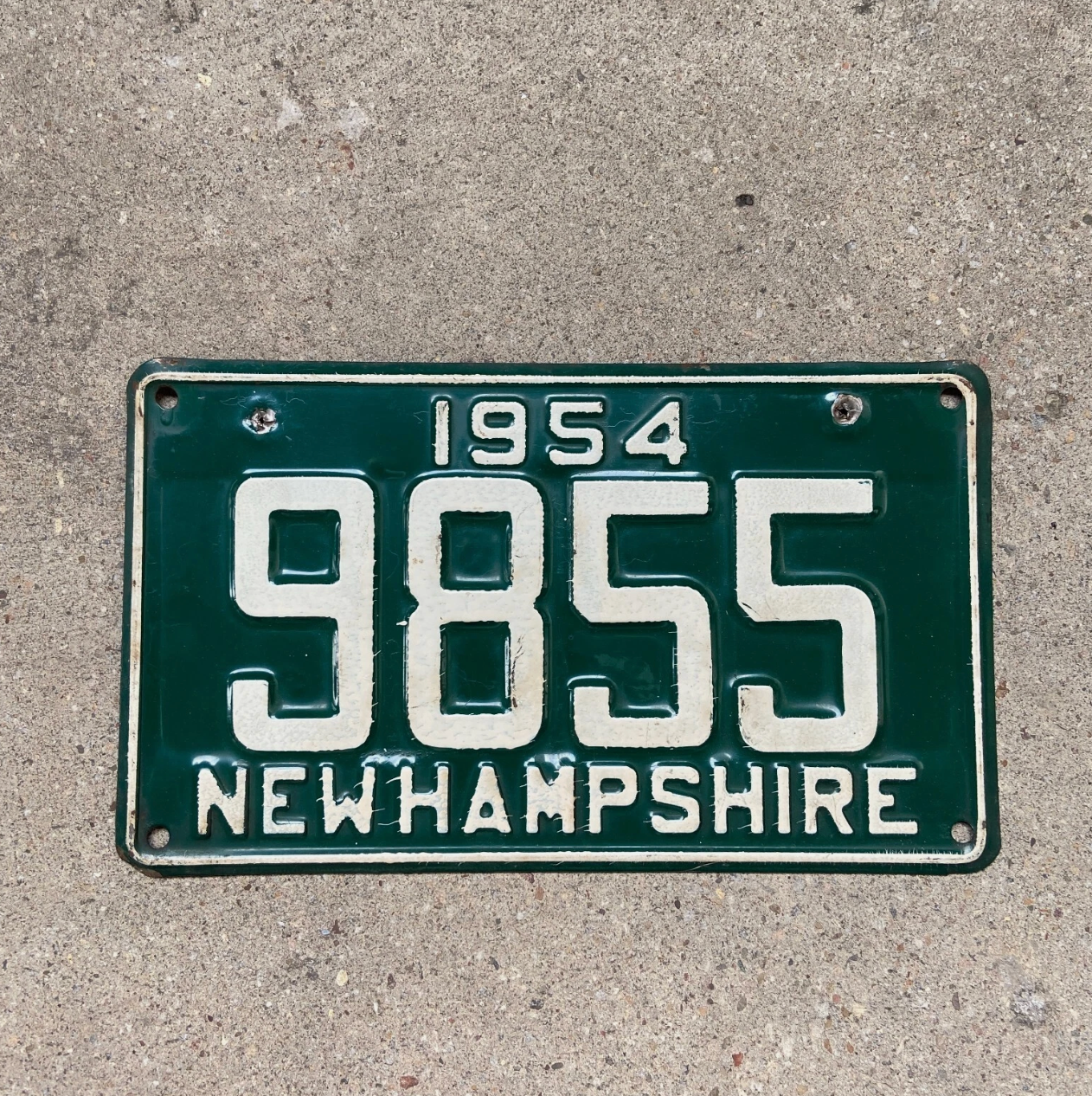 Vintage 1954 New Hampshire license plate with registration number 9855 on a concrete surface