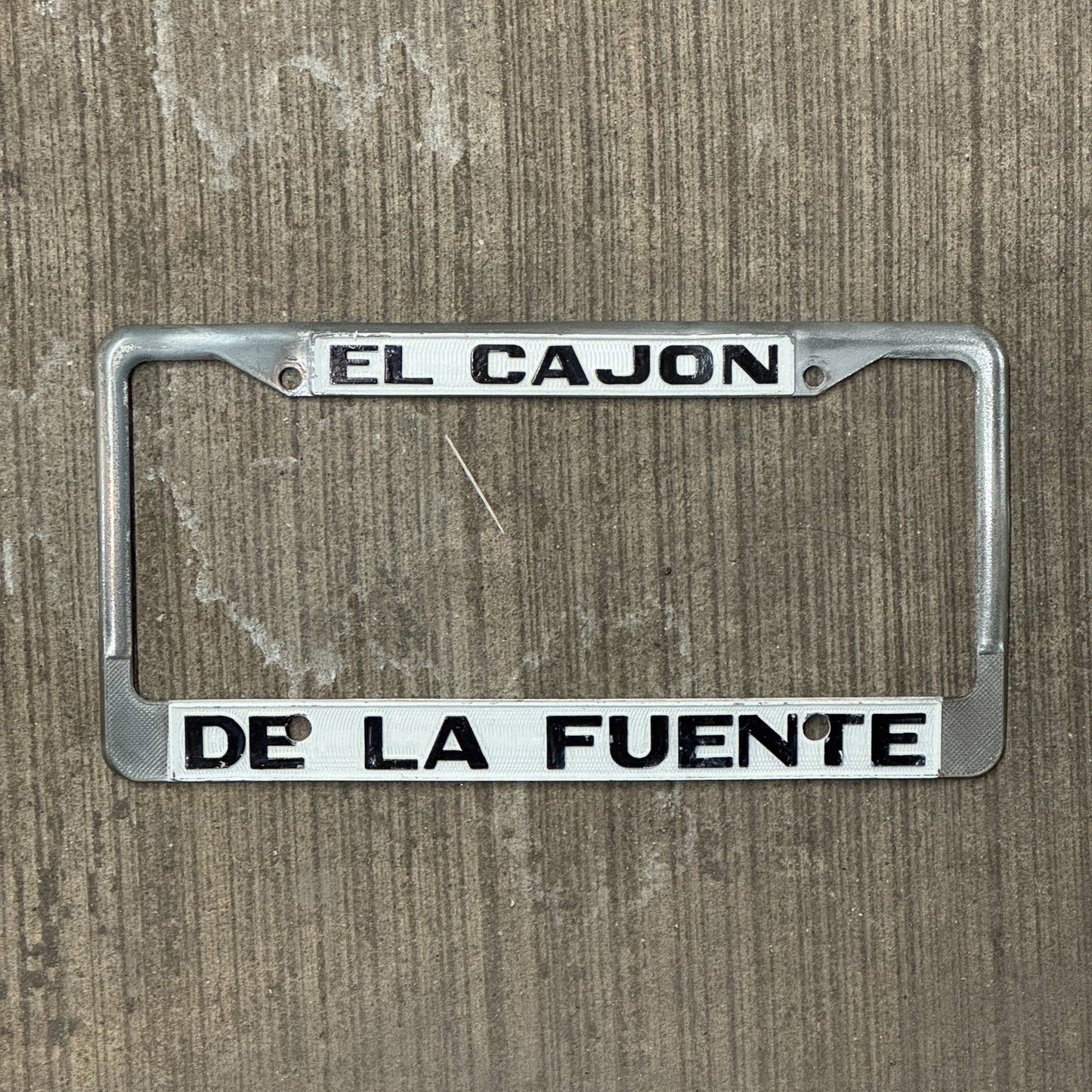 Photo of a 1970 Era California License Plate Frame Auto Tag Garage Decor Vintage Cadillac Dealer Metal El Cajon De La Fuente with original patina