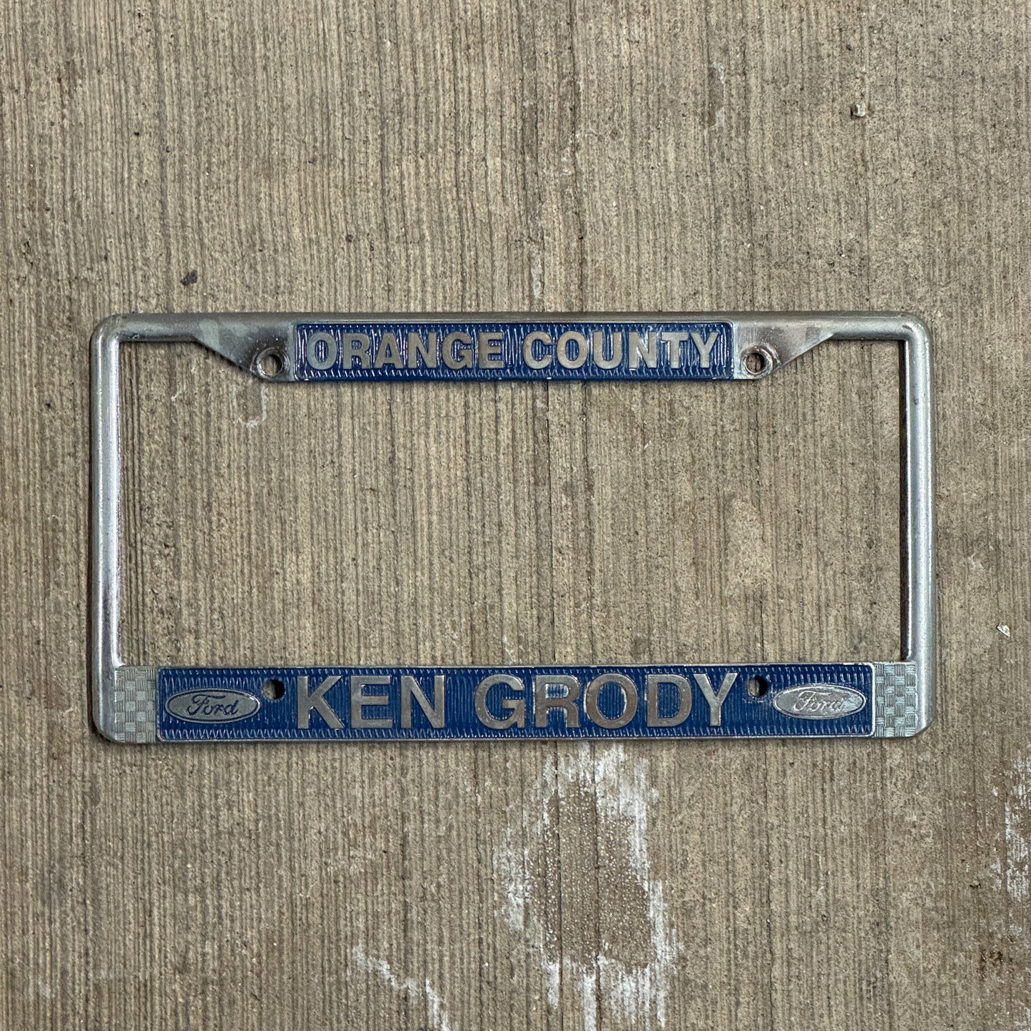 Photo of a 1970 Era California License Plate Frame Auto Tag Garage Decor Vintage Orange County Metal Ken Grody Ford with original patina