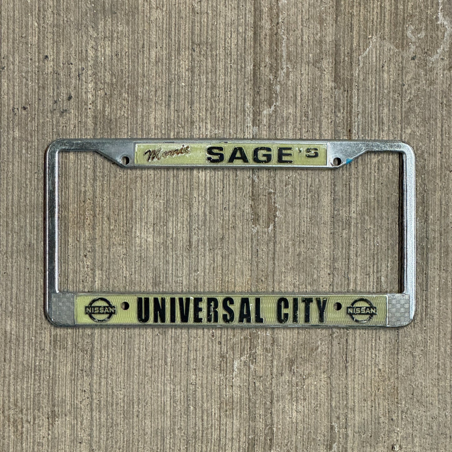 Photo of a 1980 Era California License Plate Frame Auto Tag Garage Decor Vintage Los Angeles LA Metal Morrie Sage's Universal City Nissan with original patina