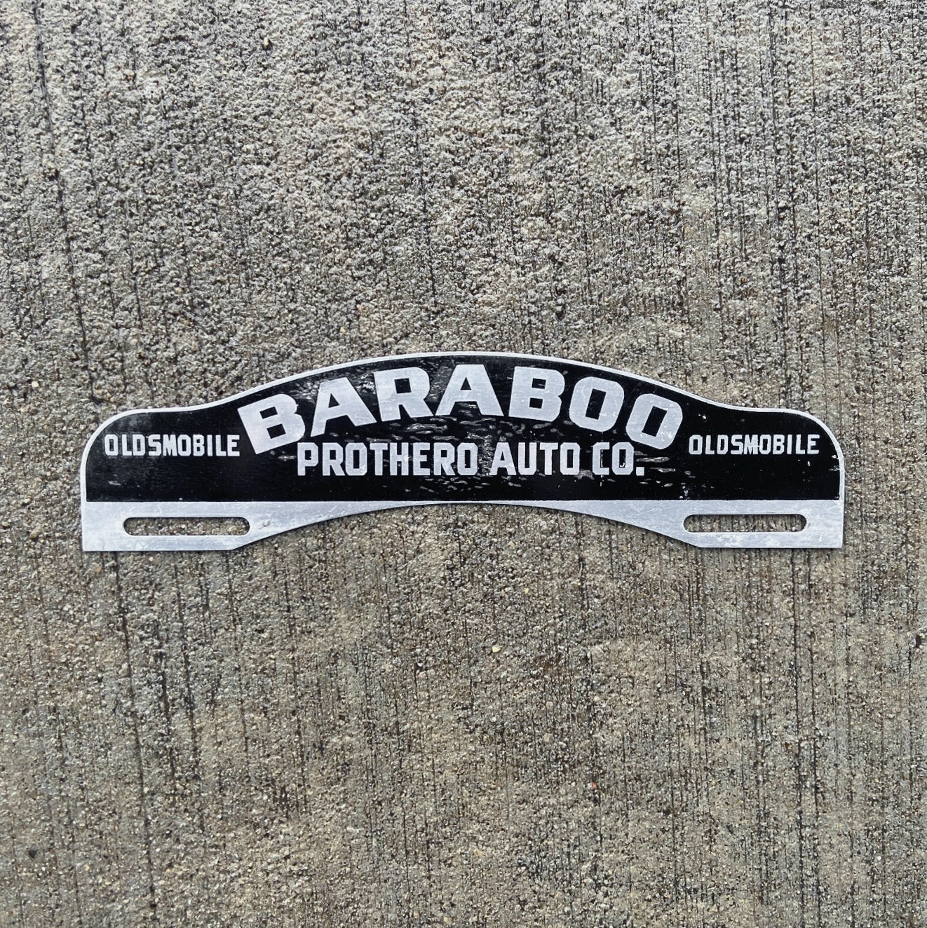 Photo of a 1950 Era Baraboo Wisconsin License Plate Topper Auto Tag Garage Decor Vintage Oldsmobile Dealer Prothero Auto with original patina