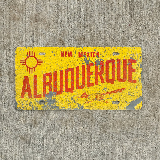 Albuquerque New Mexico booster license plate with roadrunner and zia. Set on a concrete background.