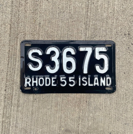 Photo of a 1955 Rhode Island license plate on a concrete background.