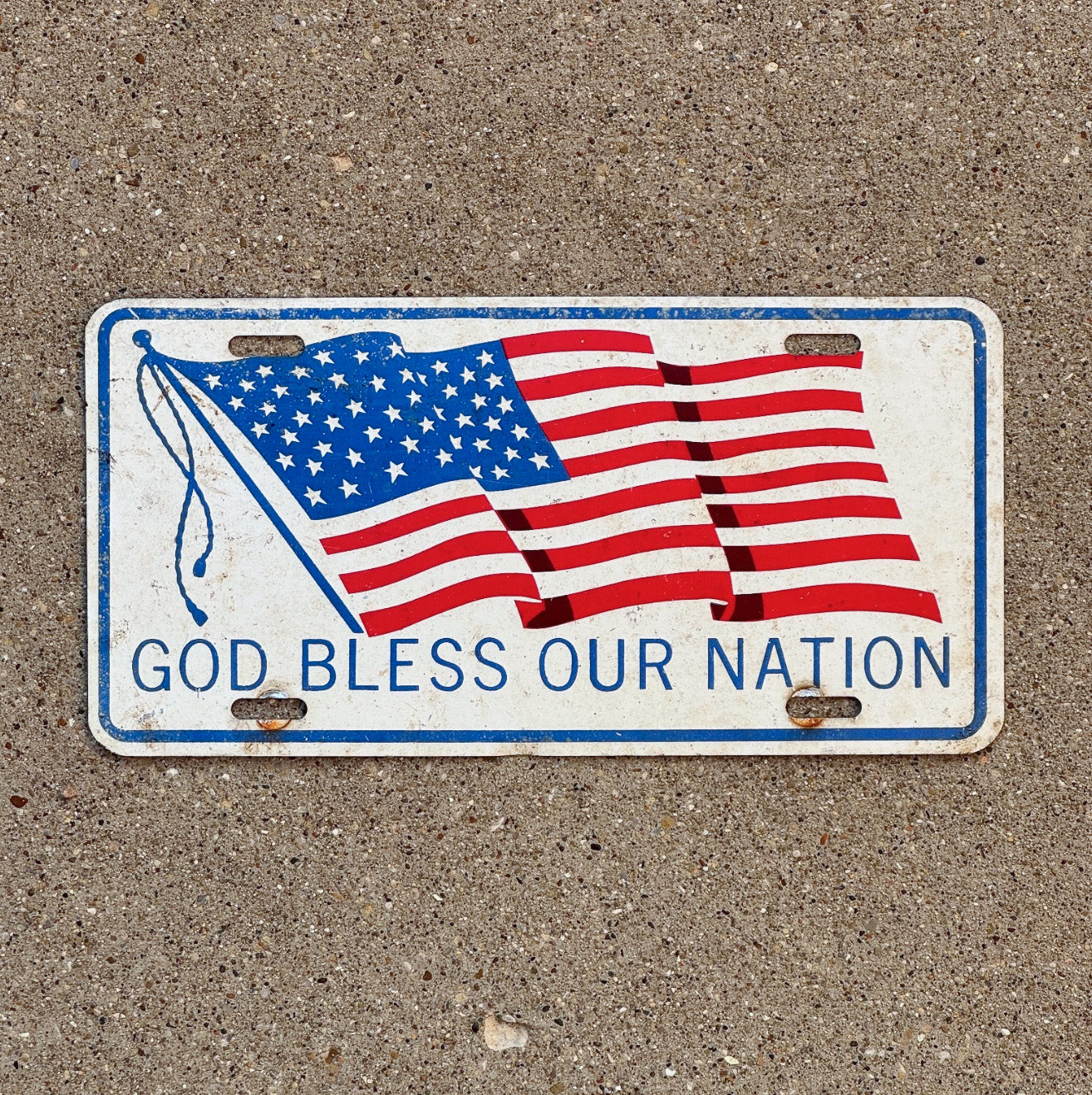 Photo of a 1960 Era God Bless Our Nation Booster License Plate Auto Tag Garage Decor Vintage Patriotic American Flag USA God Bless Our Nation with original patina