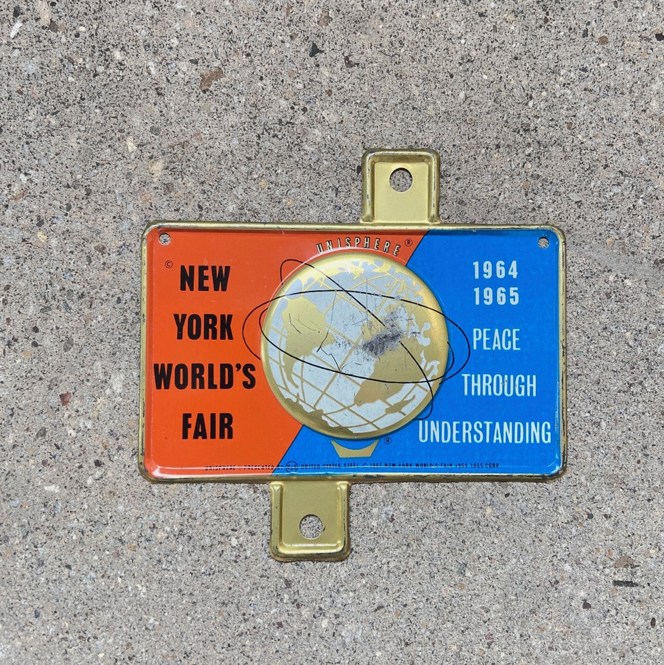 Photo of a 1964 New York World's Fair New York License Plate Topper Auto Tag Garage Decor Vintage Unisphere Embossed with original patina