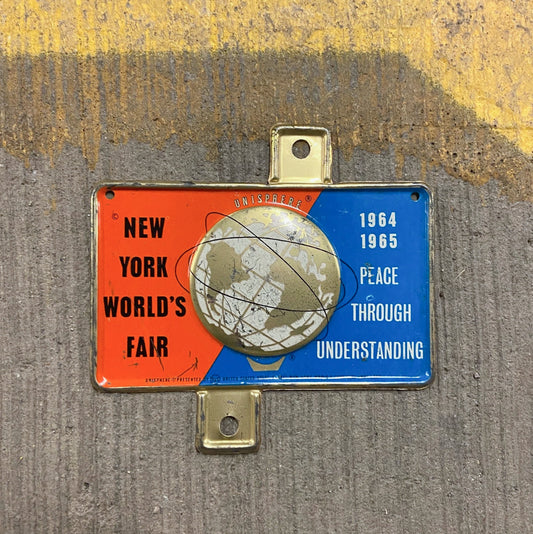 Photo of a 1964 New York World's Fair New York License Plate Topper Auto Tag Garage Decor Vintage Unisphere Embossed with original patina