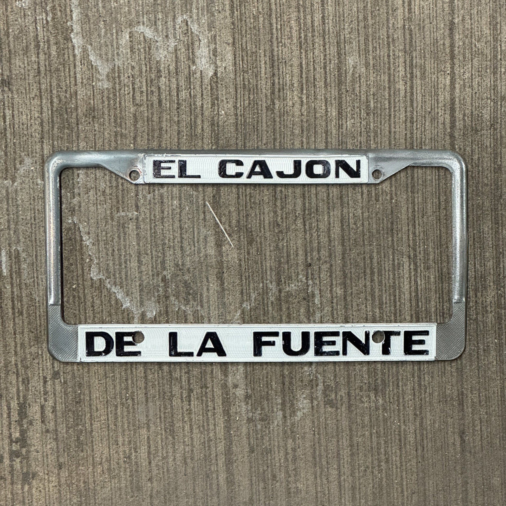 Photo of a 1970 Era California License Plate Frame Auto Tag Garage Decor Vintage Cadillac Dealer Metal El Cajon De La Fuente with original patina