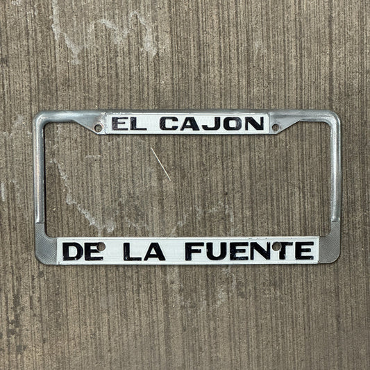 Photo of a 1970 Era California License Plate Frame Auto Tag Garage Decor Vintage Cadillac Dealer Metal El Cajon De La Fuente with original patina