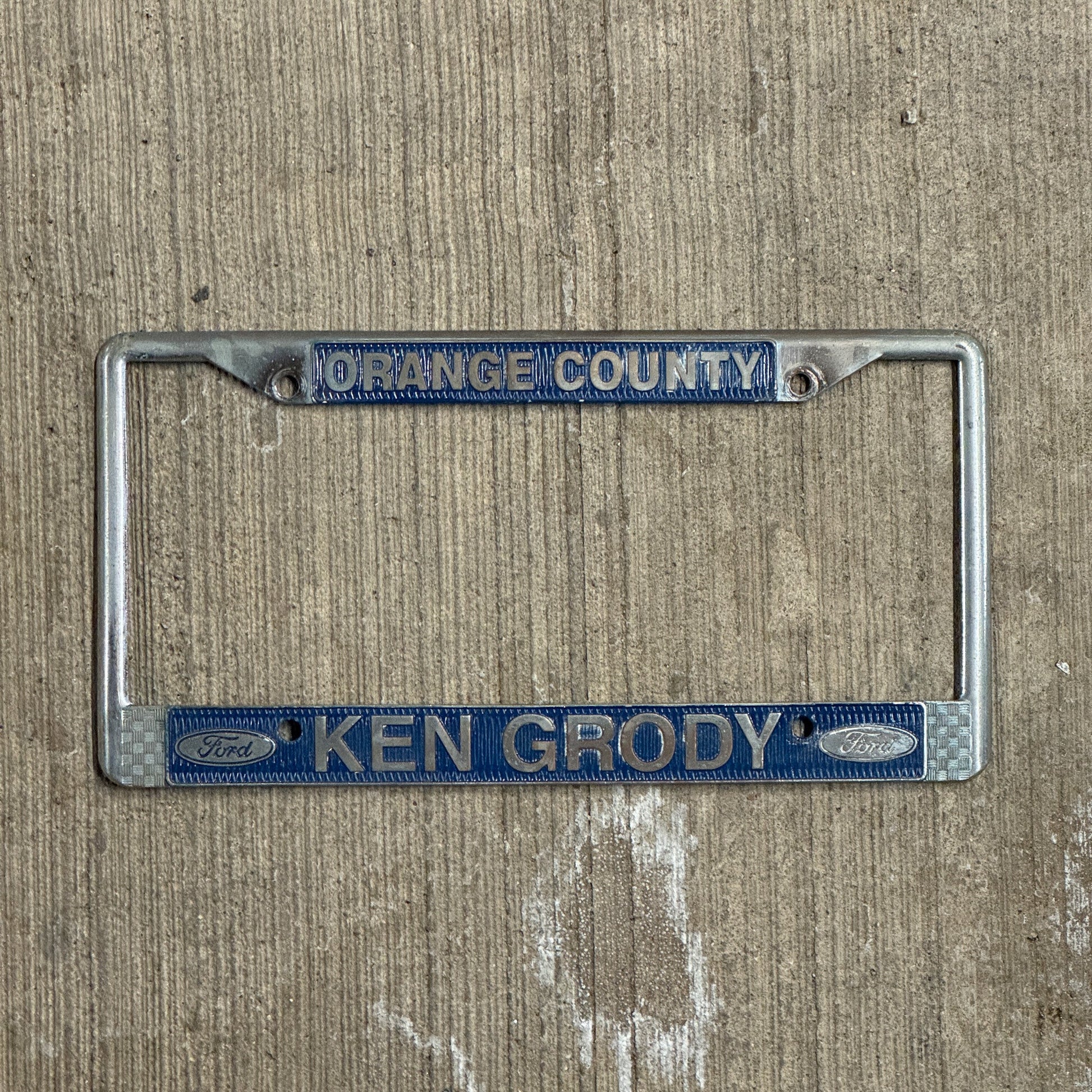Photo of a 1970 Era California License Plate Frame Auto Tag Garage Decor Vintage Orange County Metal Ken Grody Ford with original patina