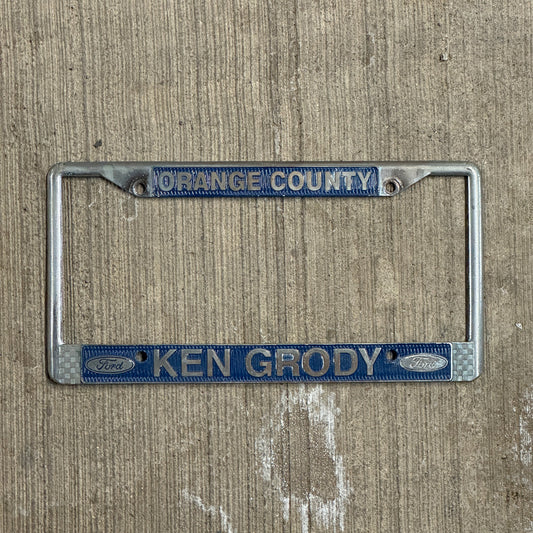 Photo of a 1970 Era California License Plate Frame Auto Tag Garage Decor Vintage Orange County Metal Ken Grody Ford with original patina