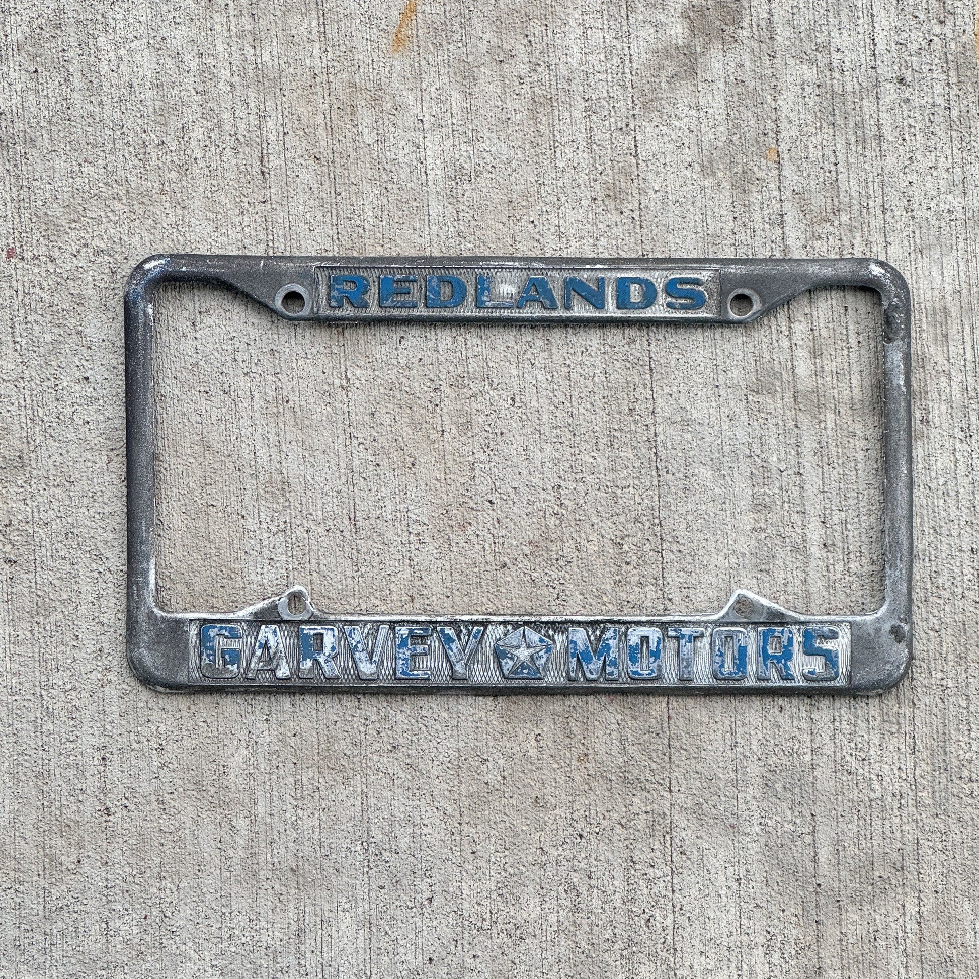 Photo of a 1970 Era California License Plate Frame Auto Tag Garage Decor Vintage Redlands Garvey Motors Chrysler and Plymouth with original patina