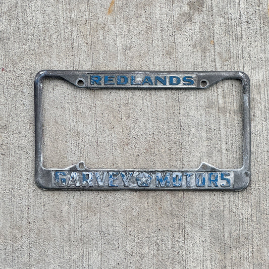 Photo of a 1970 Era California License Plate Frame Auto Tag Garage Decor Vintage Redlands Garvey Motors Chrysler and Plymouth with original patina