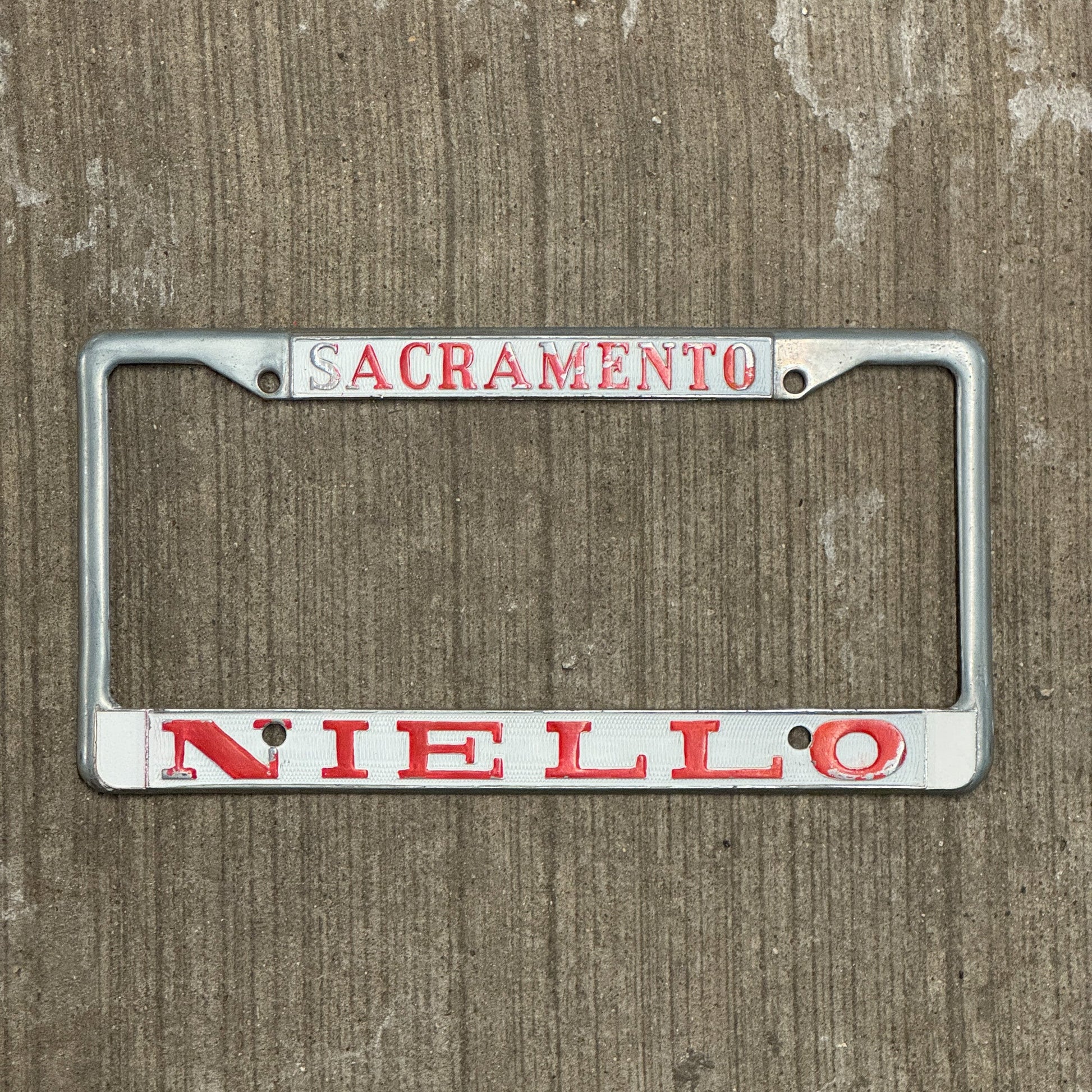 Photo of a 1970 Era California License Plate Frame Auto Tag Garage Decor Vintage Sacramento Metal Niello BMW Dealer with original patina