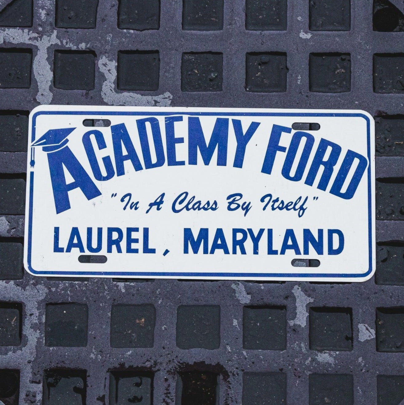 Photo of a 1970 Era Ford Laurel Maryland Booster License Plate Auto Tag Garage Decor Vintage Dealer Dealership Academy MD with original patina