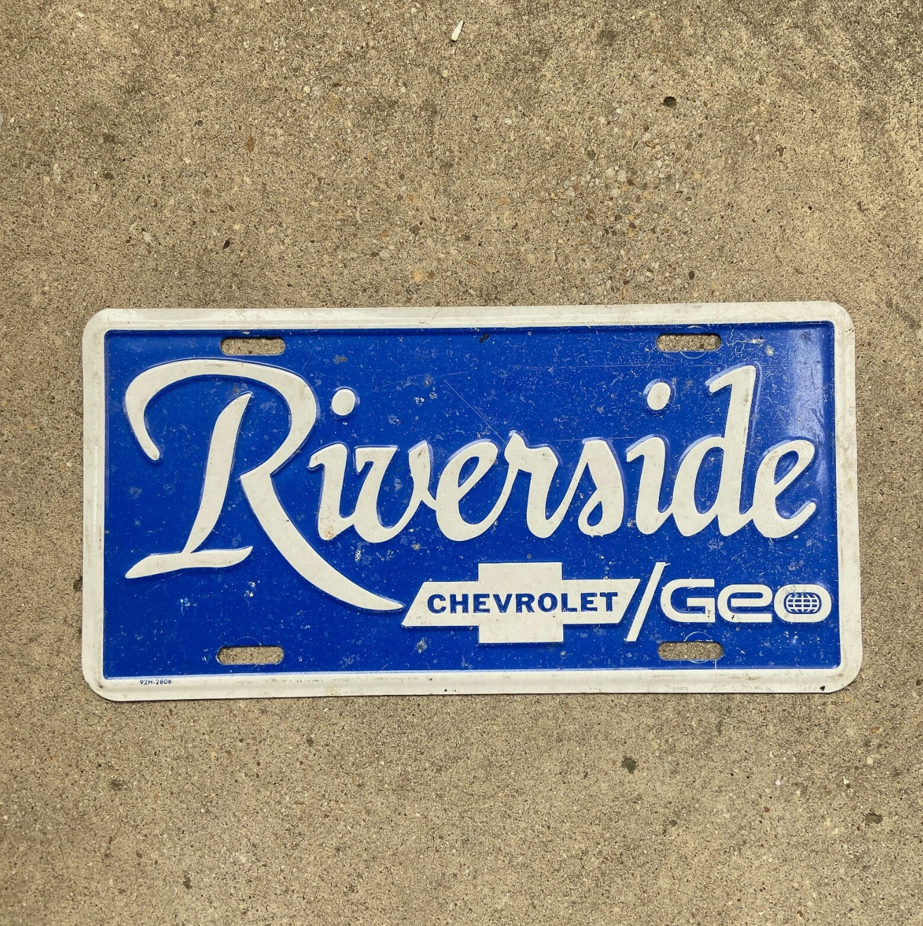 Photo of a 1970 Era Riverside Chevy Geo Booster License Plate Auto Tag Garage Decor Vintage Dealer Chevrolet Embossed Metal with original patina