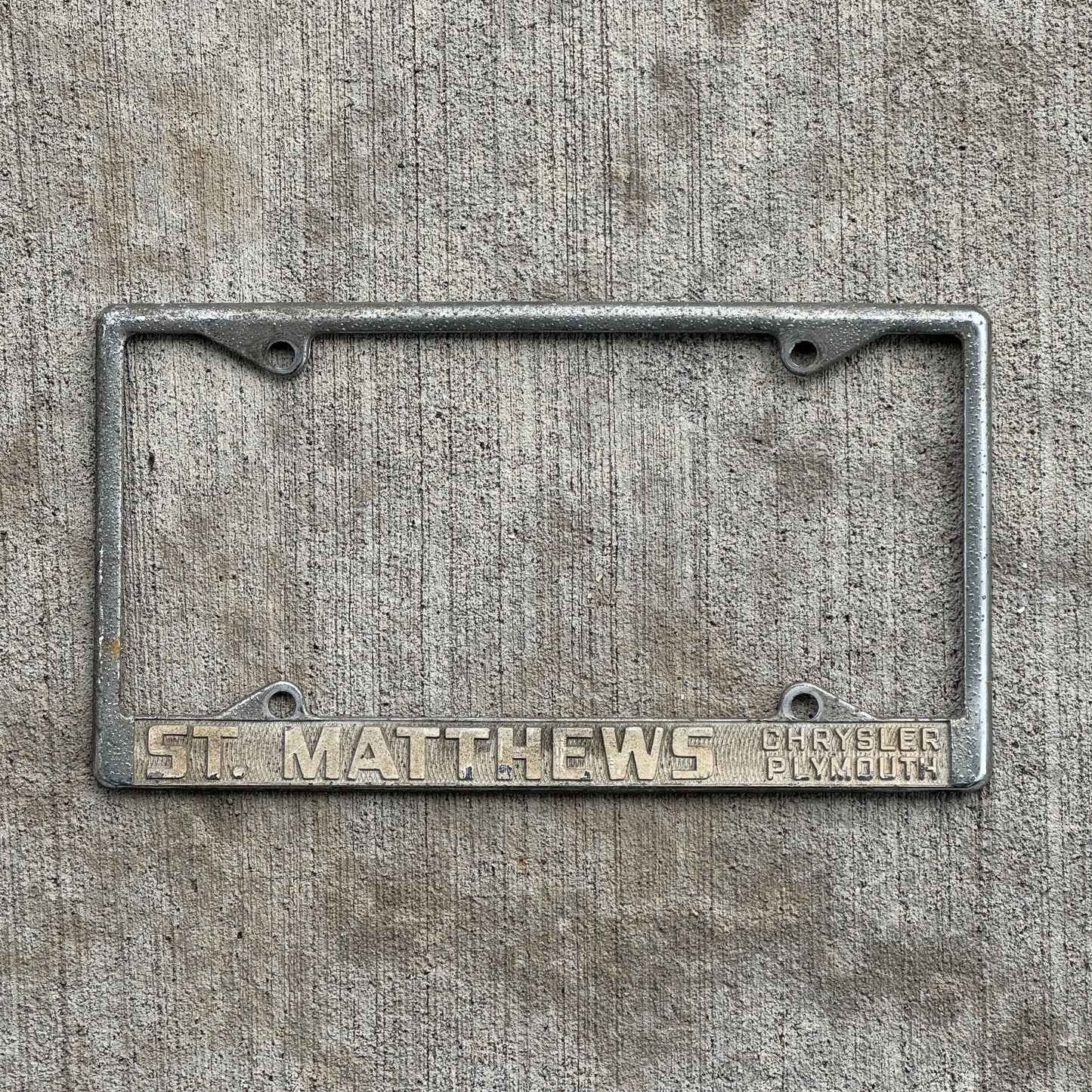 Photo of a 1970 Era St Matthews Kentucky License Plate Frame Auto Tag Garage Decor Vintage Chrysler Plymouth Dealer with original patina
