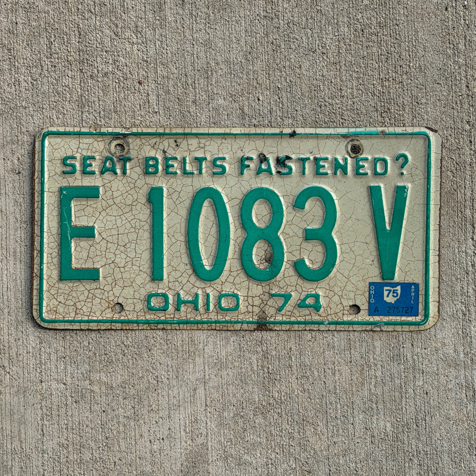 Image of 1974 1975 Ohio License Plate Auto Tag E 1083 V on a concrete background.