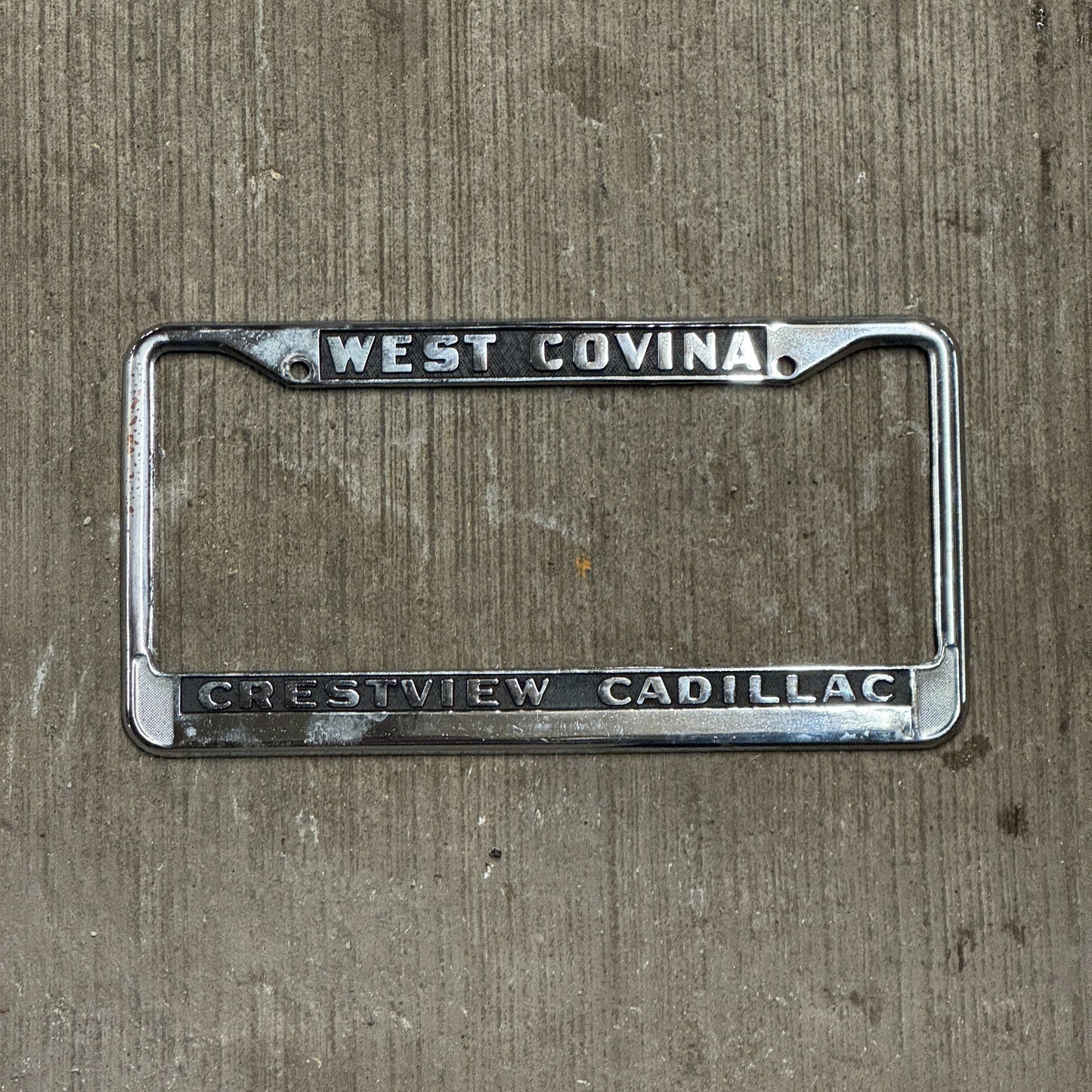 Photo of a 1980 Era California License Plate Frame Auto Tag Garage Decor Vintage West Covina Metal Crestview Cadillac with original patina