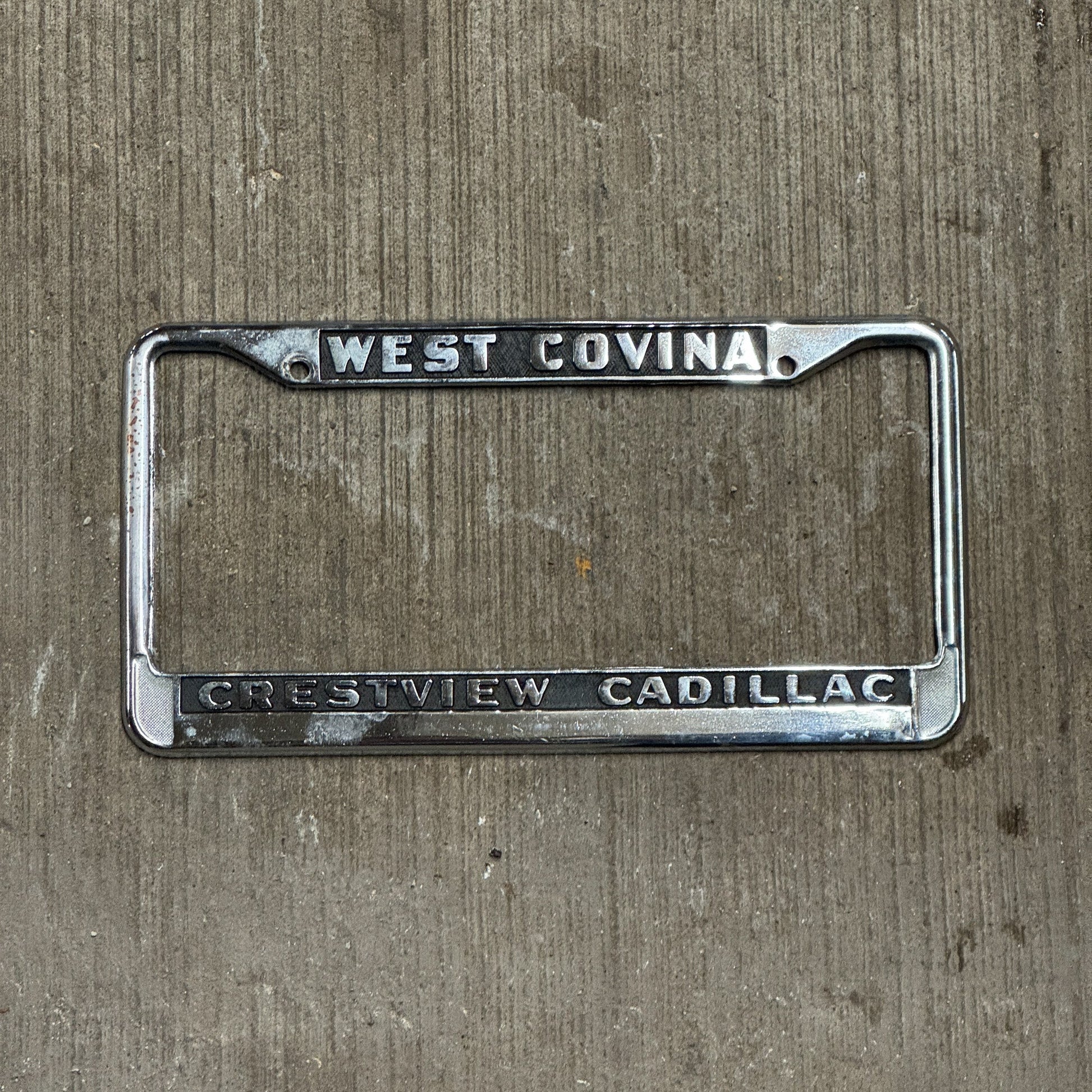 Photo of a 1980 Era California License Plate Frame Auto Tag Garage Decor Vintage West Covina Metal Crestview Cadillac with original patina