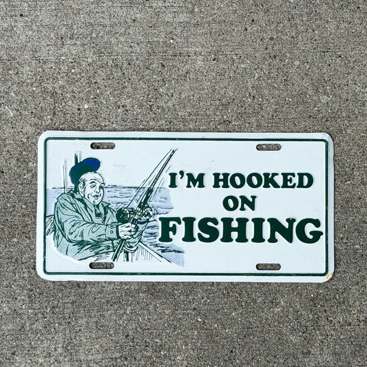 Photo of a 1980 Era I'm Hooked On Fishing Booster License Plate Auto Tag 1 Vintage Garage
 Fish Gift Metal with original patina