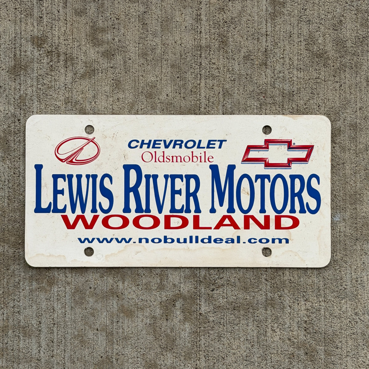 Photo of a 1980 Era Woodland Washington Booster License Plate Auto Tag Garage Decor Vintage Lewis River Motors Chevy Oldsmobile Plastic with original patina