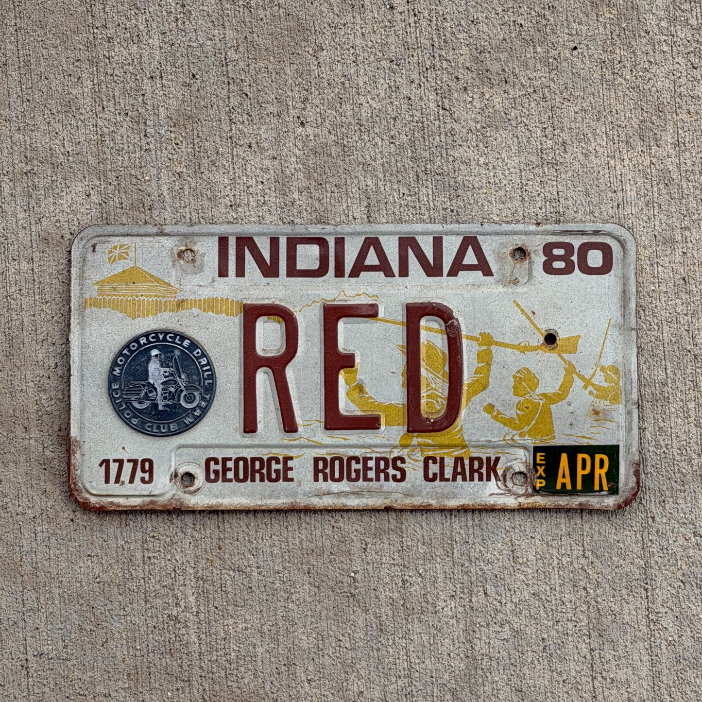 1980 Indiana license plate with RED as text on a concrete background.