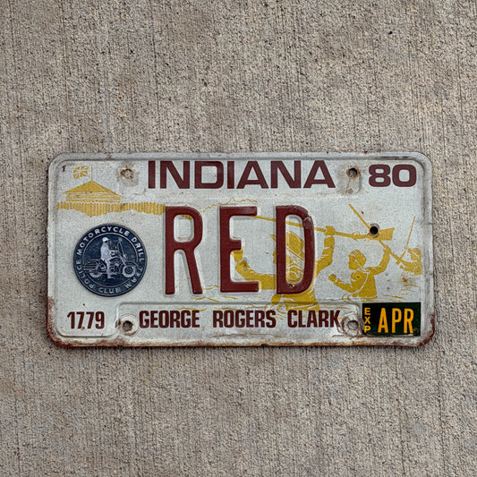 1980 Indiana license plate with RED as text on a concrete background.