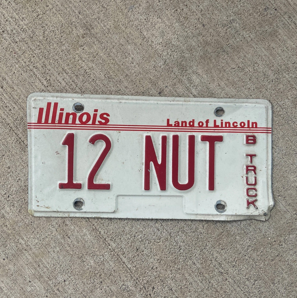 Photo of a 1985 Illinois Truck License Plate Auto Tag Garage Decor Vintage Nutty Crazy Gag Gift 12 NUT with original patina