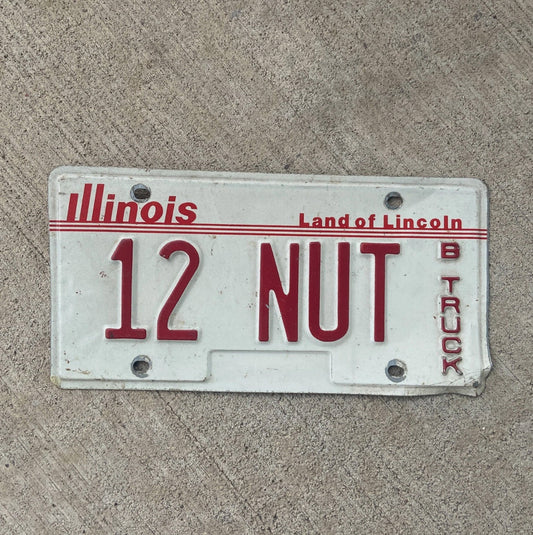 Photo of a 1985 Illinois Truck License Plate Auto Tag Garage Decor Vintage Nutty Crazy Gag Gift 12 NUT with original patina