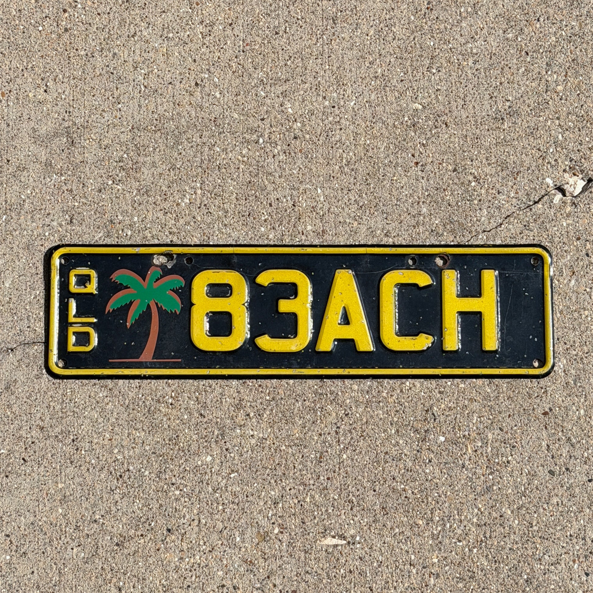 Photo of a 1990 Era Australia Graphic / Specialty License Plate Auto Tag Garage Decor Vintage Queensland BEACH Palm Tree Tropical 83ACH with original patina