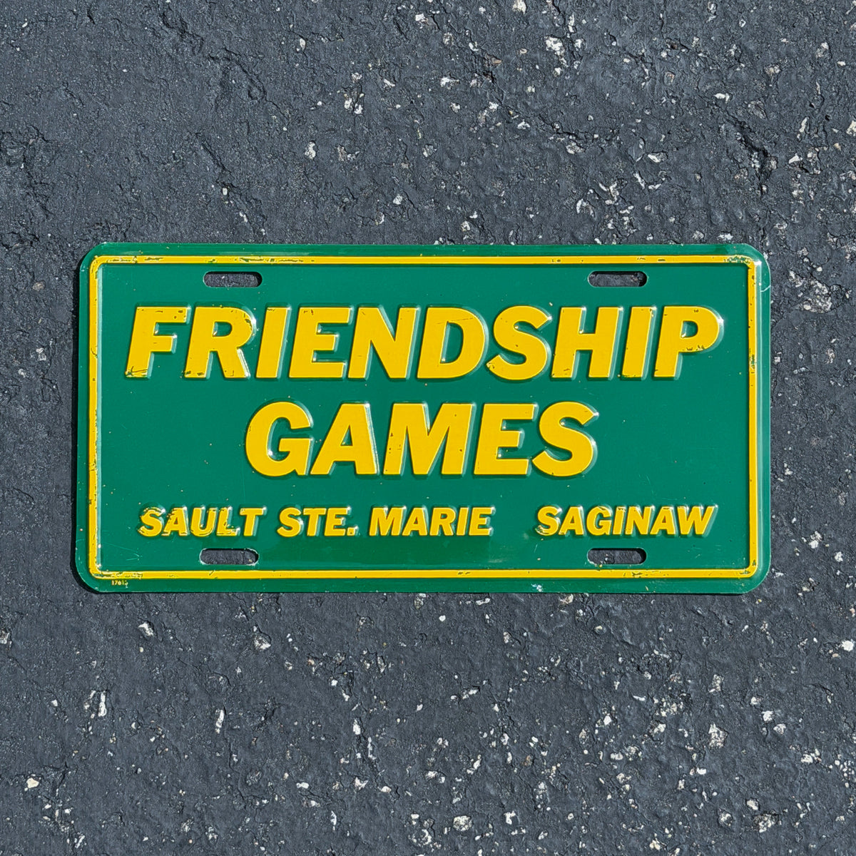 Photo of a 1990 Era Friendship Games Sault Ste Marie Saginaw Michigan Booster License Plate Auto Tag Garage Decor Vintage
 Metal with original patina