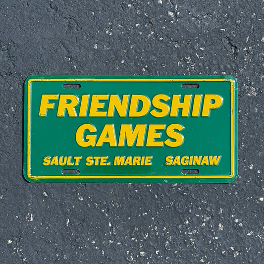 Photo of a 1990 Era Friendship Games Sault Ste Marie Saginaw Michigan Booster License Plate Auto Tag Garage Decor Vintage
 Metal with original patina