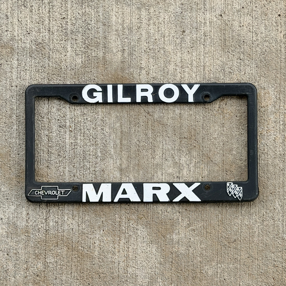 Photo of a 1990 Era Gilroy California Dealer License Plate Frame Auto Tag Garage Decor Vintage
 Plastic Marx Chevrolet Chevy Buick with original patina