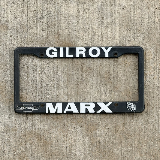 Photo of a 1990 Era Gilroy California Dealer License Plate Frame Auto Tag Garage Decor Vintage
 Plastic Marx Chevrolet Chevy Buick with original patina