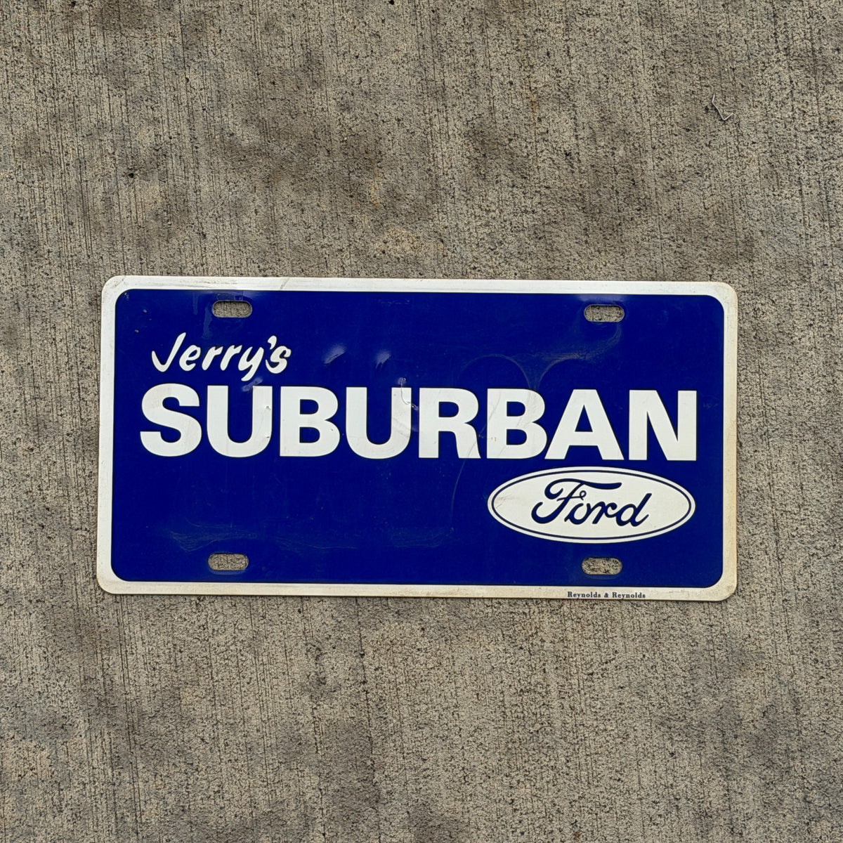 Photo of a 1990 Era Jerry's Suburban Ford Booster License Plate Auto Tag Garage Decor Vintage Plastic with original patina