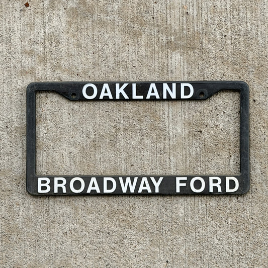 Photo of a 1990 Era Oakland California Dealer License Plate Frame Auto Tag Garage Decor Vintage
 Plastic Broadway Ford with original patina