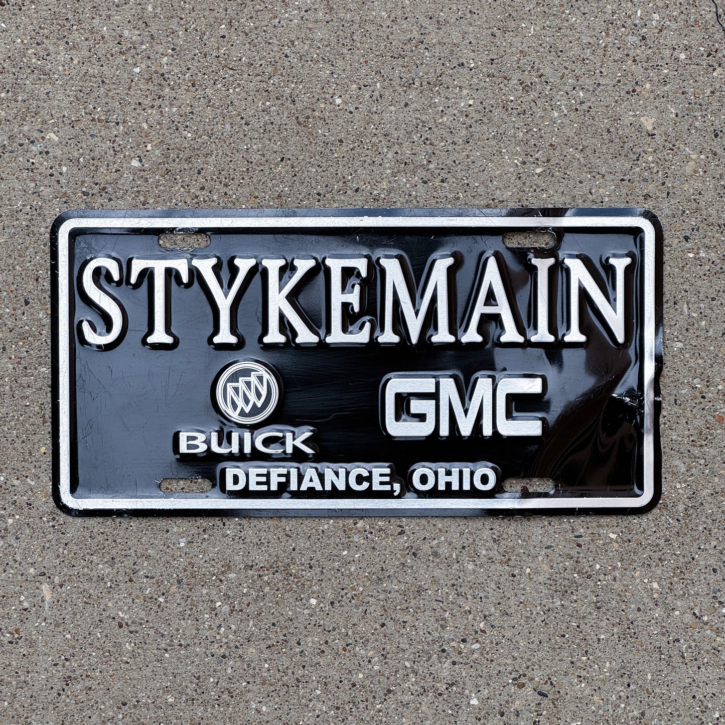 Photo of a 1990 Era Ohio Booster License Plate Auto Tag Garage Decor Vintage Buick GMC Dealer Stykeman Buick and GMC Defiance OH with original patina