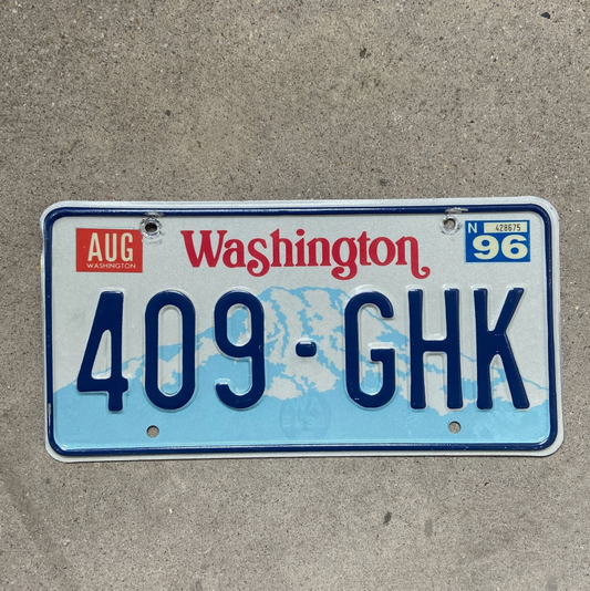 Photo of a 1990 Washington License Plate 409 GHK with 1996 registration sticker on a concrete background.