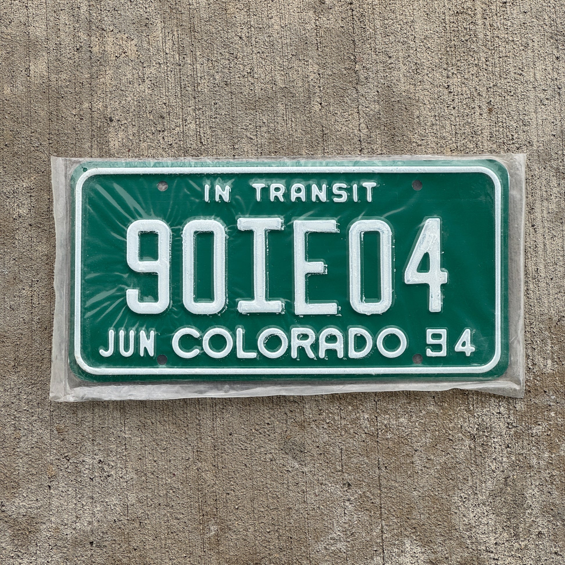 Photo of a 1994 Colorado In Transit Dealer License Plate Auto Tag Garage Decor Vintage New Old Stock NOS 90 IE 04 with original patina