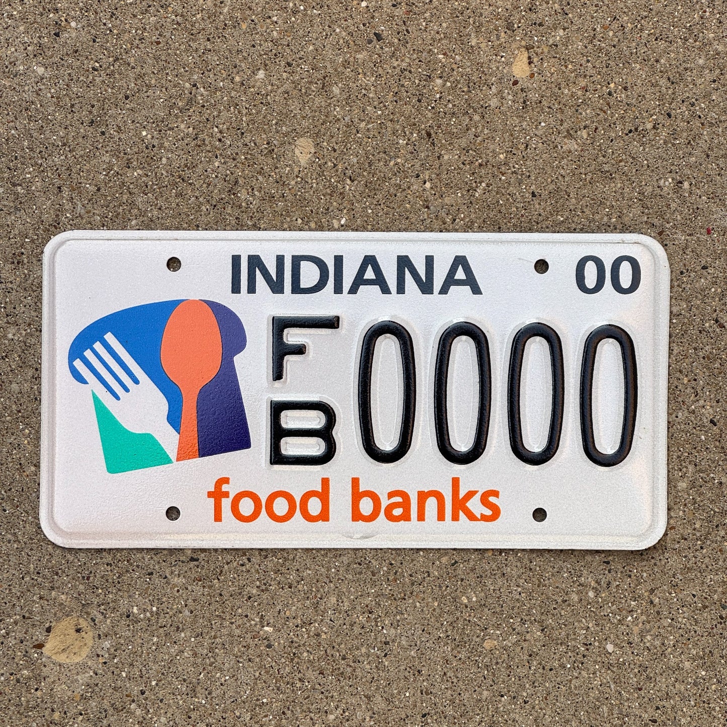 Photo of a 1999 2000 Indiana Graphic Sample License Plate Auto Tag Garage Decor Vintage Food Banks FB 0000 with original patina