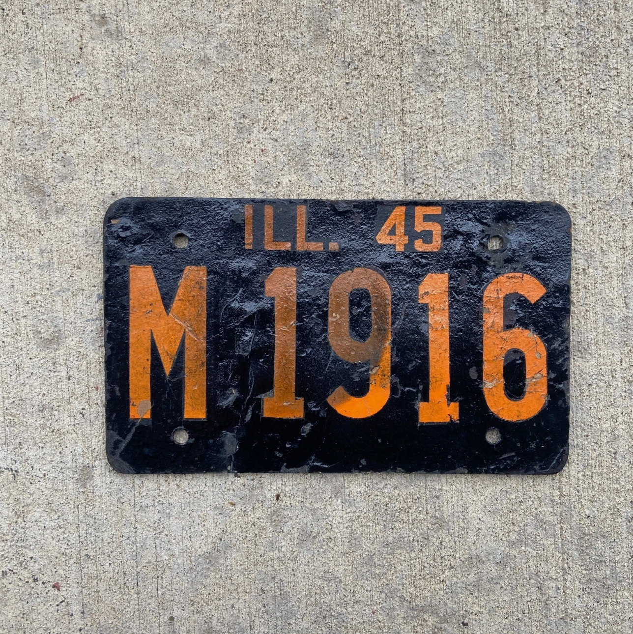Vintage 1945 Illinois municipal fiberboard license plate with wear on a concrete surface